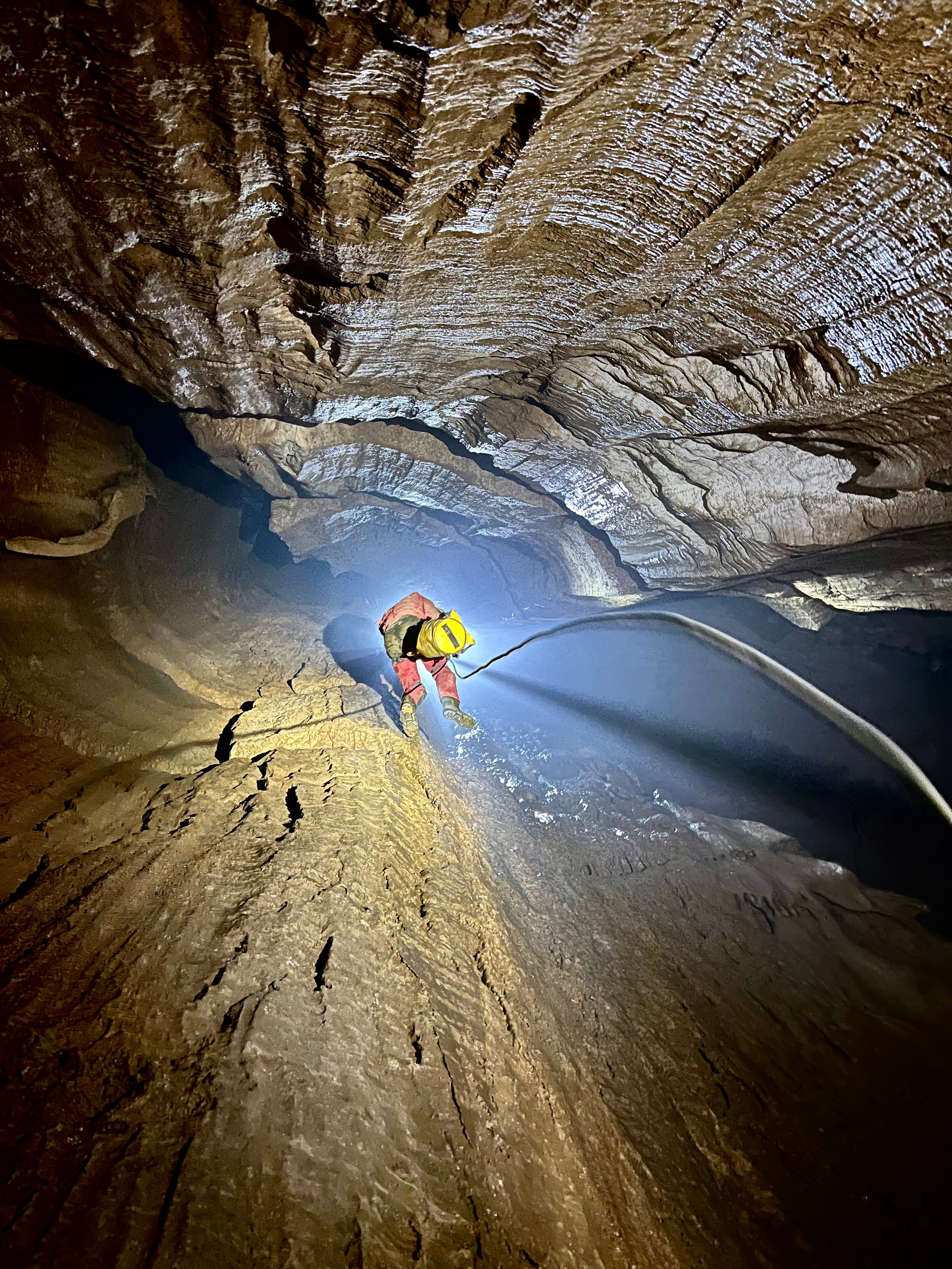Spéléologie Grenoble - Spéléologue descendant en rappel dans une grande cavité souterraine, éclairé par un faisceau lumineux, photo par Eva Lourau